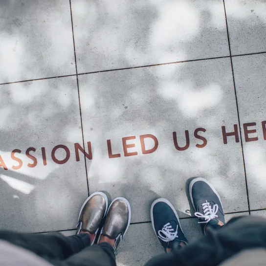 Feet stand by words painted on the ground that read "Passion led us here"