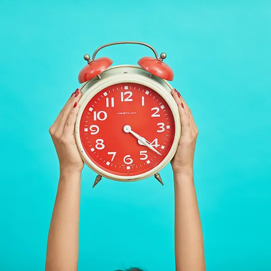 Person holding red and beige twin bell analog alarm clock
